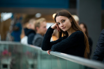 Teenager. Young pretty white caucasian teenage girl with long hair with problem skin and long hair in a shopping center near the railing.
