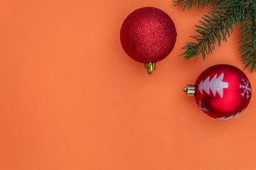 Decoration for Christmas and New Year Greeting Card With Two Red Decorative Balls and Pine Tree Branch on Orange Background. Copy Space on The Left Side
