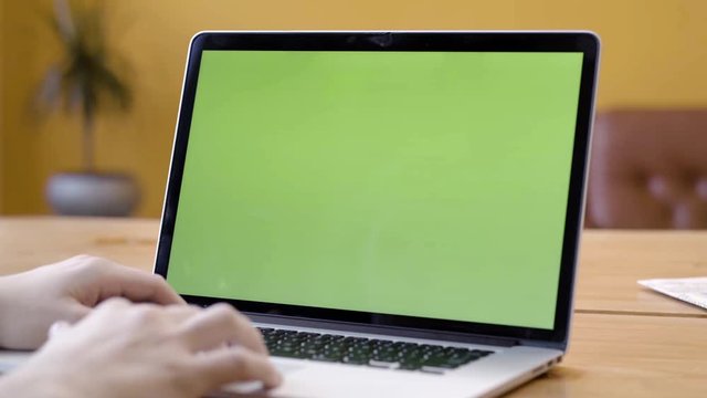 Close-up of freelancer sitting at laptop with green screen. Stock footage. Man is typing on laptop with green screen working in freelance and cozy atmosphere