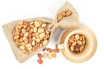 Lot of whole fresh brown bean vicia faba with jute bag , ceramic saucer and ceramic cup flatlay isolated on white background