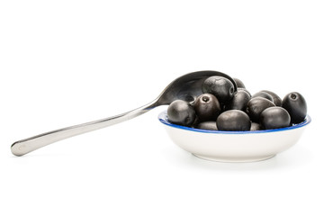 Lot of whole canned black olive on porcelain saucer with metal teaspoon isolated on white background