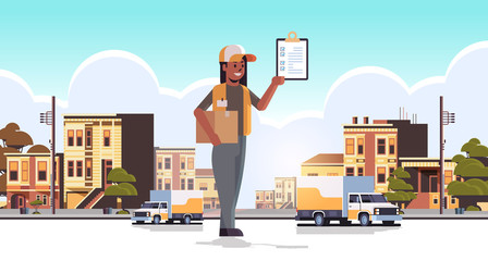postwoman in uniform holding cardboard parcel box and receiving form african american courier express delivery service concept modern city street cityscape background flat full length horizontal