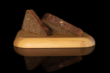 Group of two slices of fresh baked dark bread on wooden square plate isolated on black glass