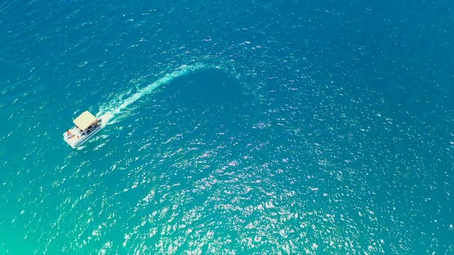 Aerial top view of a boat moving on the water of an awesome blue lagoon, drone flying from right to left - Bora Bora, French Polynesia