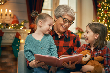Grandmother reading  to granddaughters near Christmas tree.