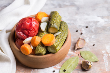 Homemade pickled tomatoes and cucumbers with carrots, garlic and Bay leaf. Blurred light background.