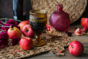 Glass of red wine, apples, grapefruits, autumn leaves and flowers on a wooden table
