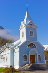Scenic wooden church painted in blue color against mountainous landscape in Northern Iceland. Icelandic traditional official building structure with framed windows and decorative bits of adornment.
