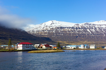 Houses in sea harbor of Norther Iceland with snowy mountains nearby. Inhabitable Icelandic landscape in springtime.