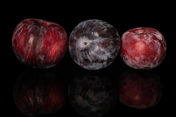 Group of three whole fresh red plum isolated on black glass