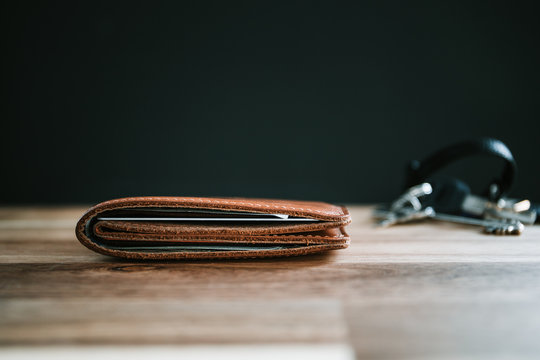 Brown leather wallet and keys on a wooden table with black background.