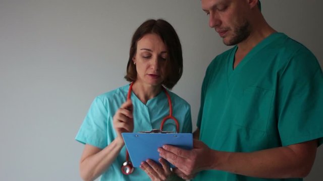 Doctor and intern, medical assistant. A female doctor signs documents in a folder in the hands of her young intern