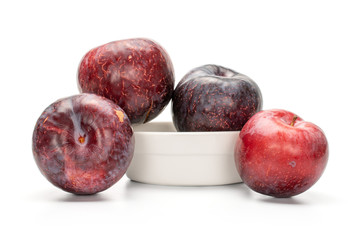 Group of four whole fresh red plum in ceramic stewpan isolated on white background