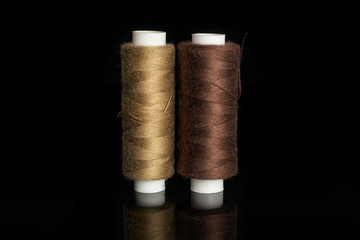 Group of two whole haberdashery item standing thread spools isolated on black glass