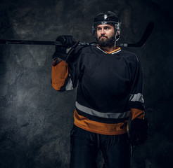 Portrait of brutal bearded man in hockey player uniform at dark photo studio.