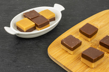 Group of eight whole sweet brown caramel chocolate candy in white oval ceramic bowl on bamboo cutting board on grey stone