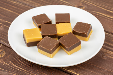 Group of eight whole sweet brown caramel chocolate candy on white ceramic plate on brown wood