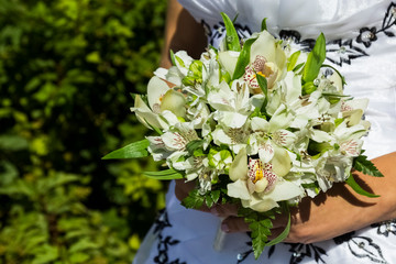 A bride in a white dress is holding a beautiful wedding bouquet. Fresh flowers