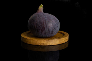 One whole fresh purple fig on bamboo coaster isolated on black glass