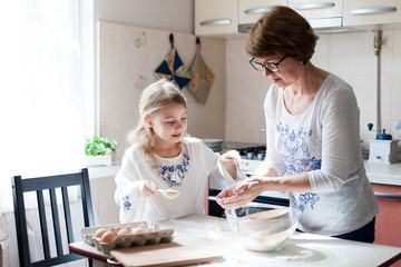 Family is cooking in cozy kitchen at home. Mother and child are making food and meal. Woman and little girl are baking pastries. Cute kid is helping to prepare dinner. Children chef concept.