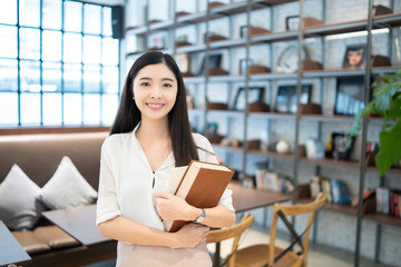 Education study abroad,Asian Chinese student girl holding book  looking to camera, happy mood smiling broadly ,she is Young female student who study in the school library copy space vintage tone