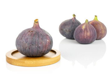 Group of four whole fresh purple fig on bamboo coaster isolated on white background