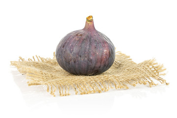 One whole fresh purple fig on natural sackcloth isolated on white background