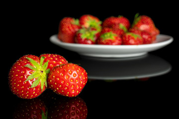 Lot of whole fresh red strawberry on white ceramic plate isolated on black glass
