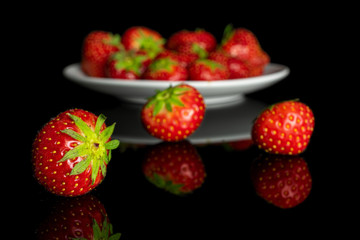 Lot of whole fresh red strawberry on white ceramic plate isolated on black glass