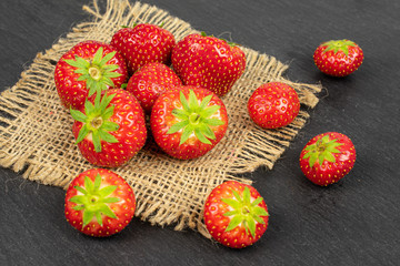 Lot of whole fresh red strawberry on natural sackcloth on grey stone