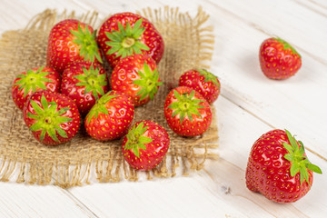 Lot of whole fresh red strawberry on natural sackcloth on white wood