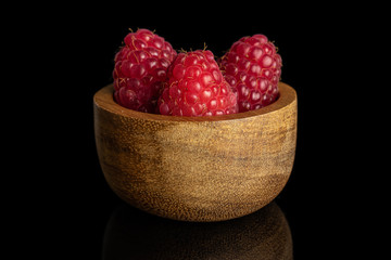 Group of three whole fresh red raspberry in tiny wooden bowl isolated on black glass