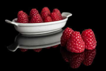 Lot of whole fresh red raspberry in white oval ceramic bowl isolated on black glass