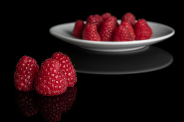 Lot of whole fresh red raspberry on white ceramic plate isolated on black glass