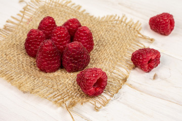 Group of ten whole fresh red raspberry on natural sackcloth on white wood