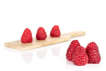 Group of six whole fresh red raspberry on small wooden cutting board isolated on white background