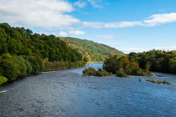 Fototapeta na wymiar Scenic view of River Tay in autumn in Dunkeld and Birnham in Perthshire in Scotland. Fall panoramic river view in Scotland. Sunny day, blue sky, October.