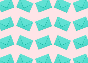 Creative pattern made of turquoise envelopes on pastel pink background.
