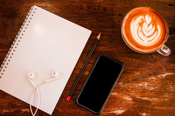 Blank notebook and smart phone with coffee on wooden table