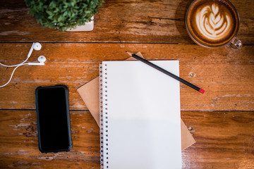 Blank notebook and smart phone with coffee on wooden table