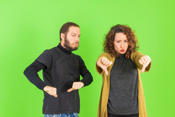 Beautiful young couple over green isolated background doing ok sign, thumb down with fingers, excellent sign