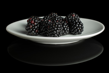 Lot of whole fresh black blackberry on white ceramic plate isolated on black glass