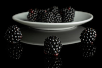 Lot of whole fresh black blackberry on white ceramic plate isolated on black glass
