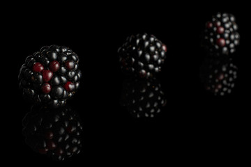 Group of three whole fresh black blackberry isolated on black glass