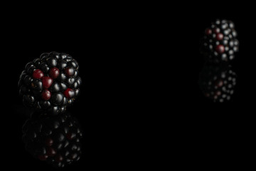 Group of two whole fresh black blackberry isolated on black glass