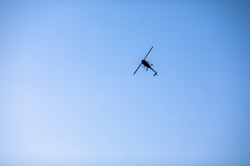 Silhouette of a chopper high in the blue sky seen from below, the military maneuvers; worm’s eye view.