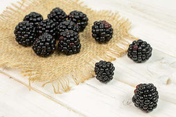Lot of whole fresh black blackberry on natural sackcloth on white wood
