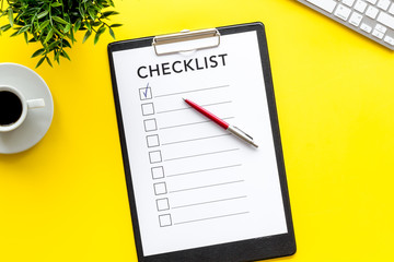 Checklist and pen on yellow office background top view copy space