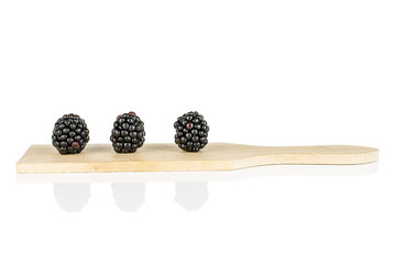 Group of three whole fresh black blackberry on small wooden cutting board isolated on white...