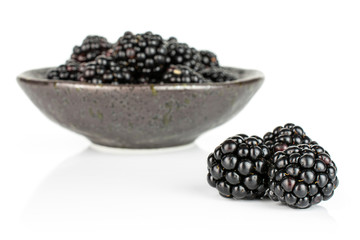 Lot of whole fresh black blackberry in dark ceramic bowl isolated on white background